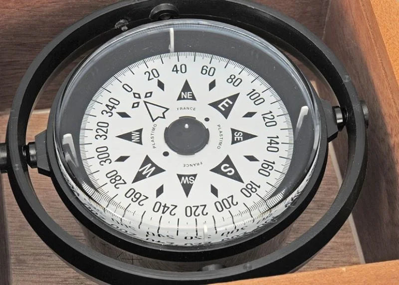 Classic marine compass with white graduated card, gimballed mount, and varnished wooden box with Plexiglas lid. Perfect for traditional boats or nautical collectors.

